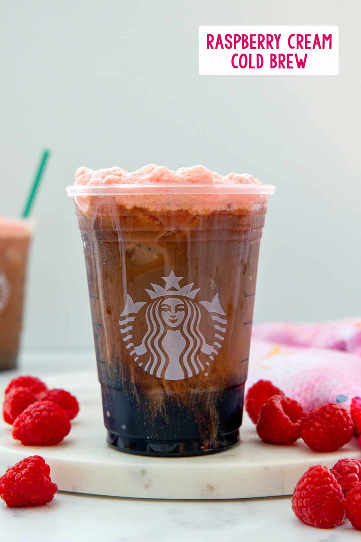 Head-on view of a raspberry cream cold brew with raspberry cold foam, fresh raspberries all around, and recipe title at top.