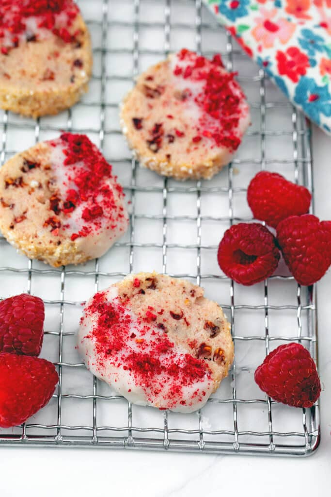 Raspberry shortbread cookies on a metal rack with fresh raspberries around.