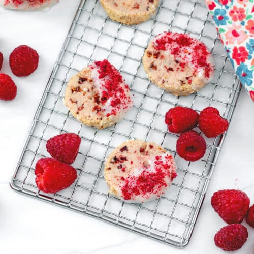 Overhead view of raspberry shortbread cookies on a metal rack with raspberries all around.
