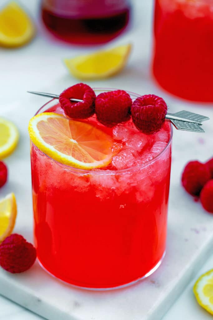Head-on view of a raspberry vodka lemonade with lemon slice and raspberries on a skewer.