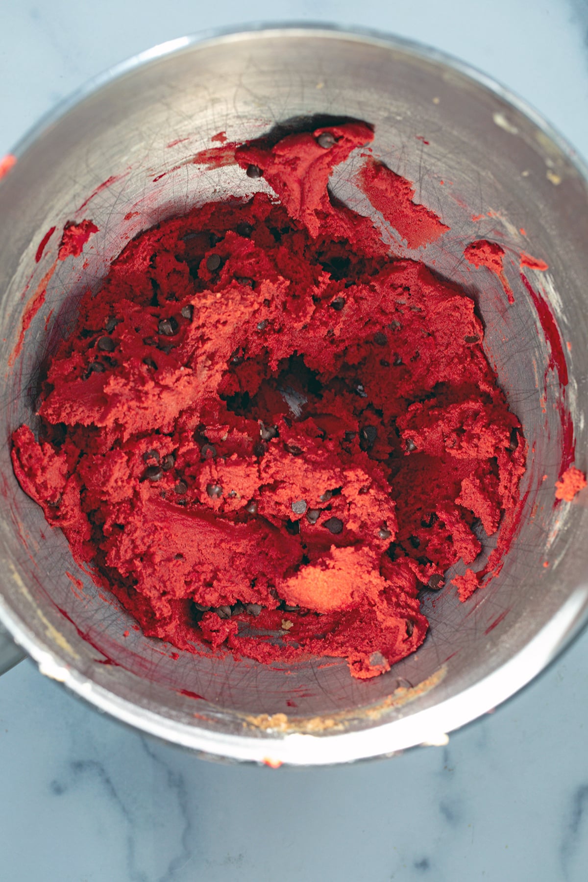 Red velvet cookie dough with chocolate chips in mixing bowl.