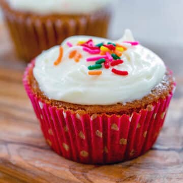 Closeup view of a red velvet cupcake with cream cheese frosting and sprinkles.
