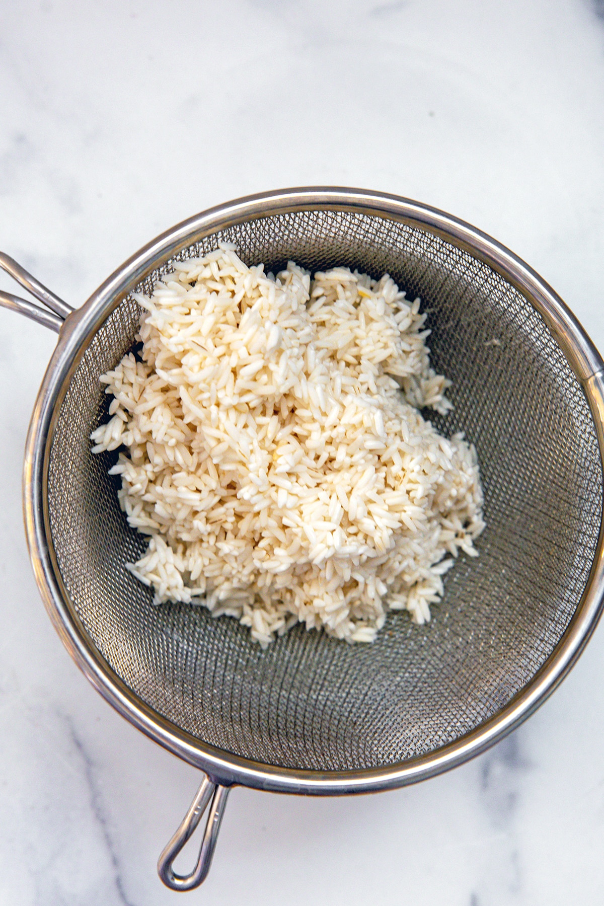 Rice being strained out of water into mesh sieve.