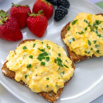 Closeup view of toast with ricotta scrambled eggs with berries in the background.