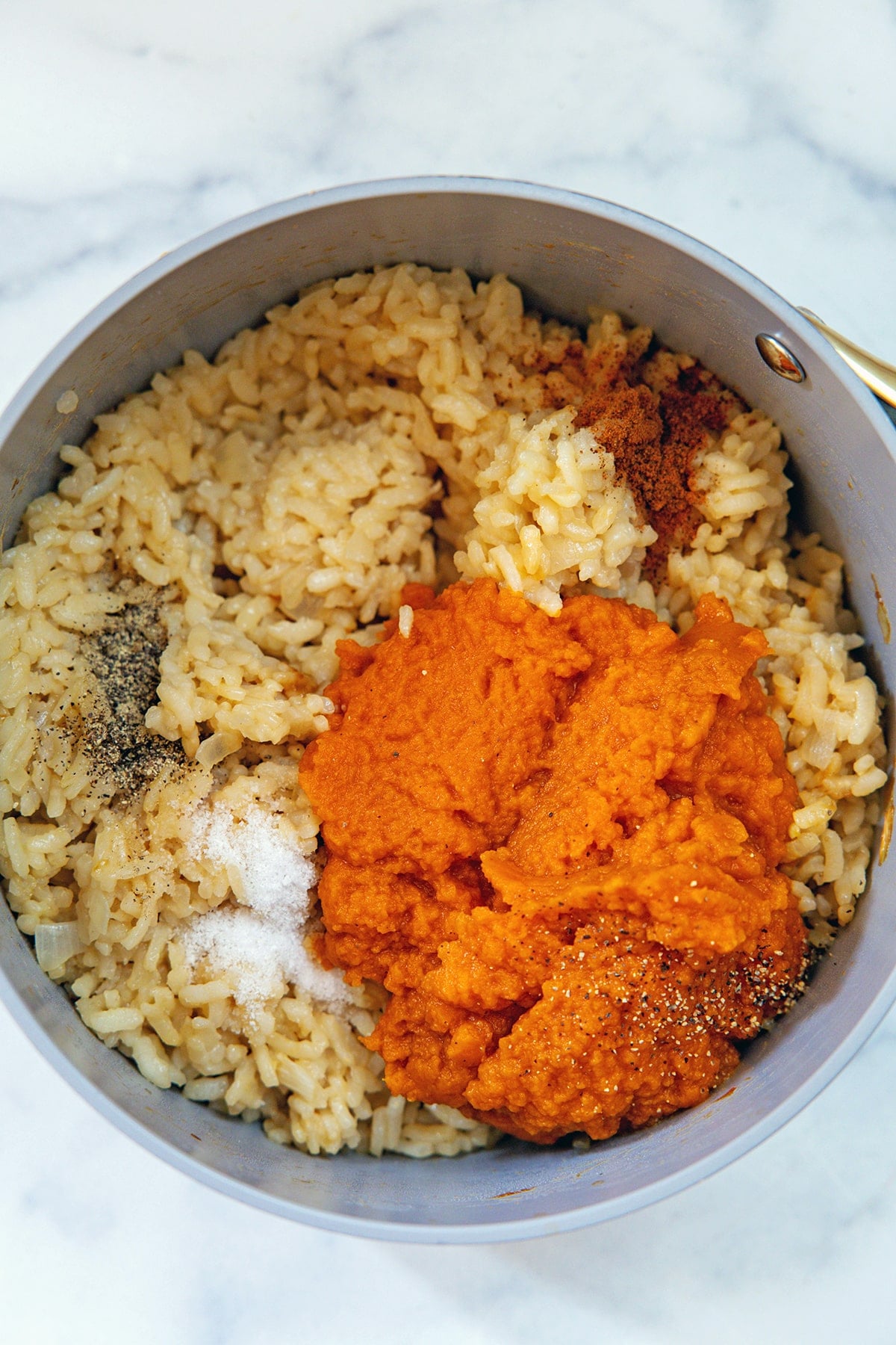 Overhead view of risotto in saucepan with pumpkin puree, salt, and pepper.