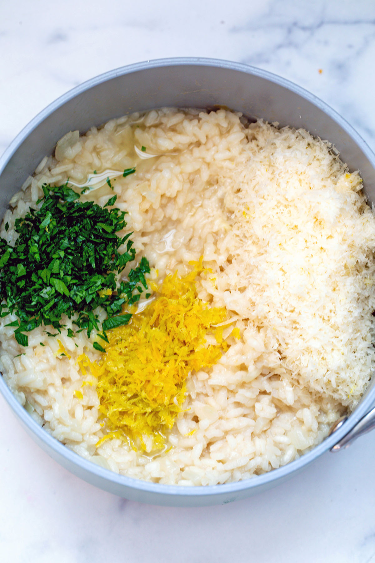 Risotto in saucepan with lemon zest, parsley, and parmesan cheese.