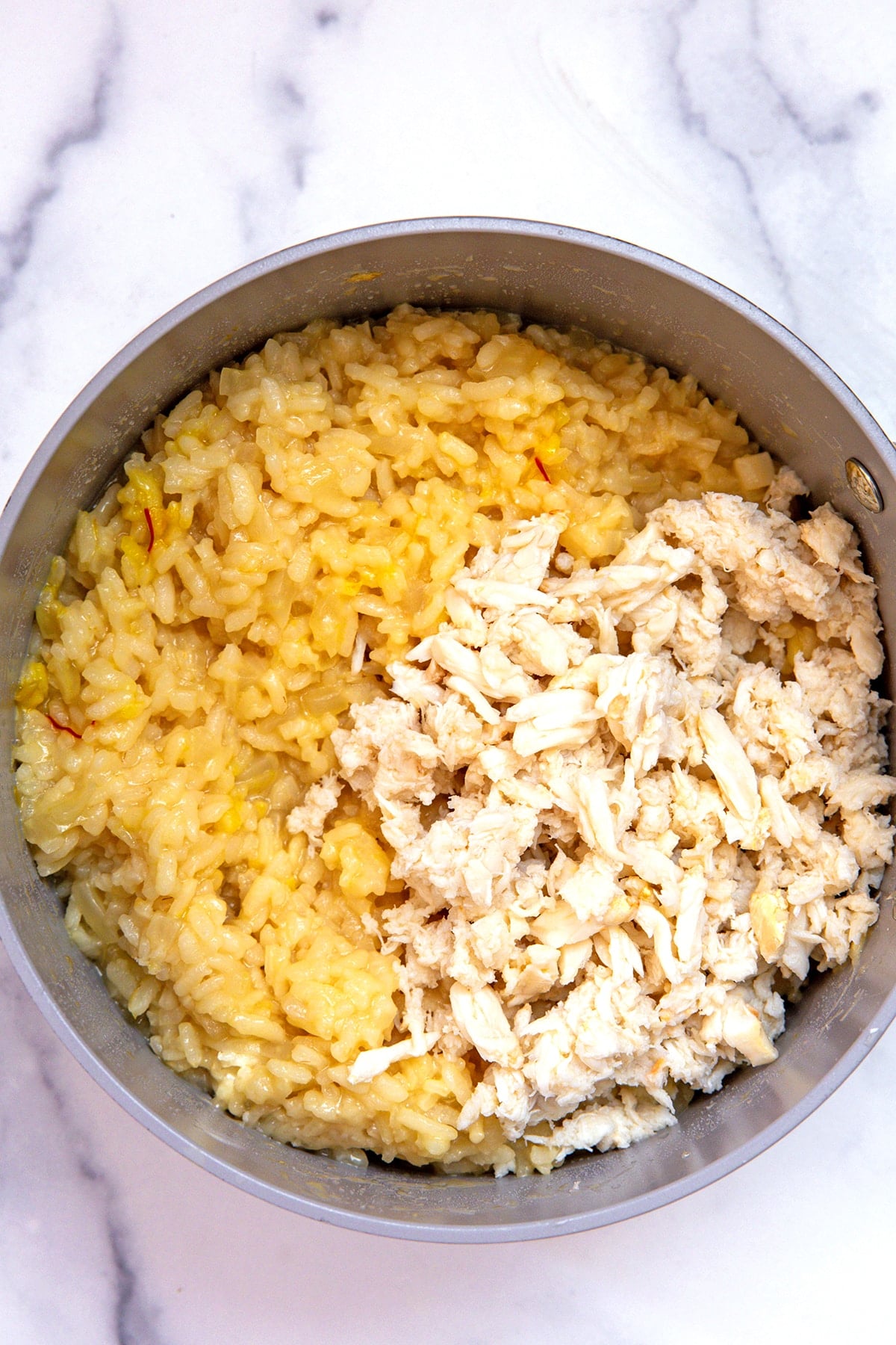 Saffron risotto topped with crab meat in saucepan.