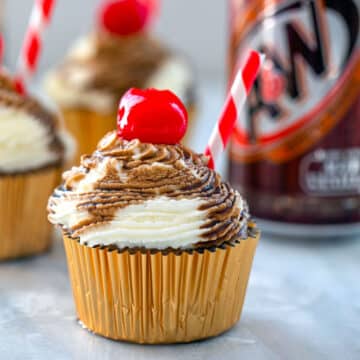 Closeup view of a root beer float cupcake with soda syrup drizzle and cherry on top.