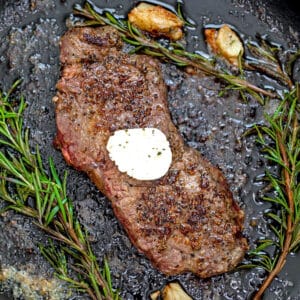 Closeup view of rosemary steak in a cast iron skillet.