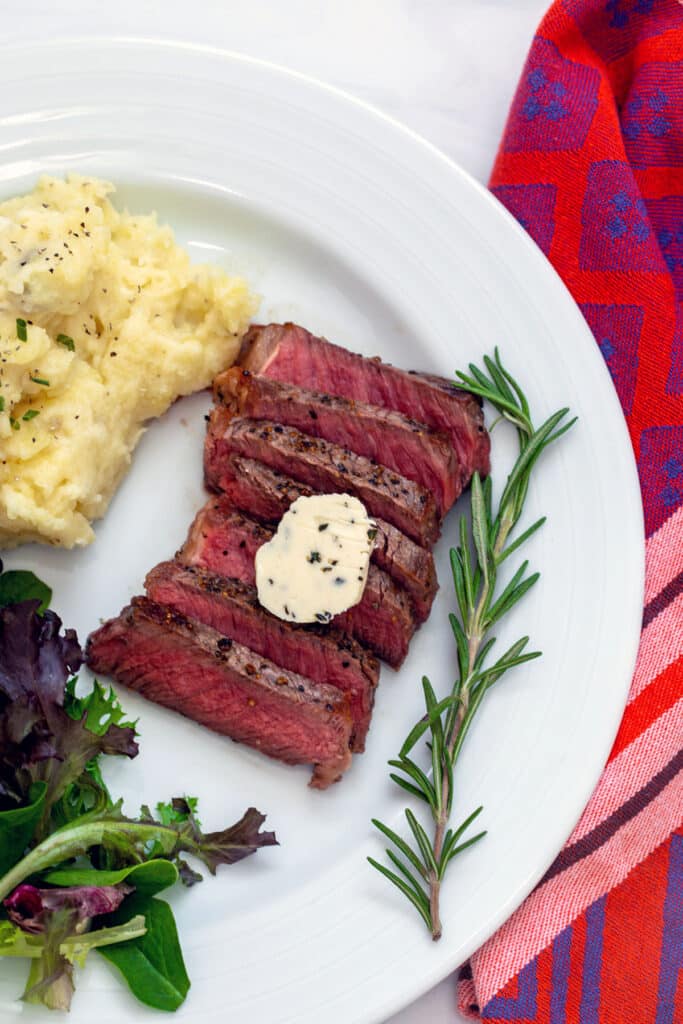Sliced rosemary steak with sprig of rosemary, mashed potatoes, and salad.