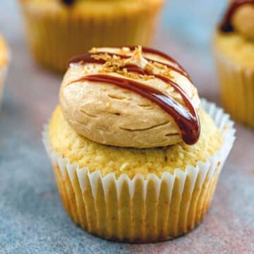 Closeup view of a salted caramel cupcake with frosting and caramel drizzle.