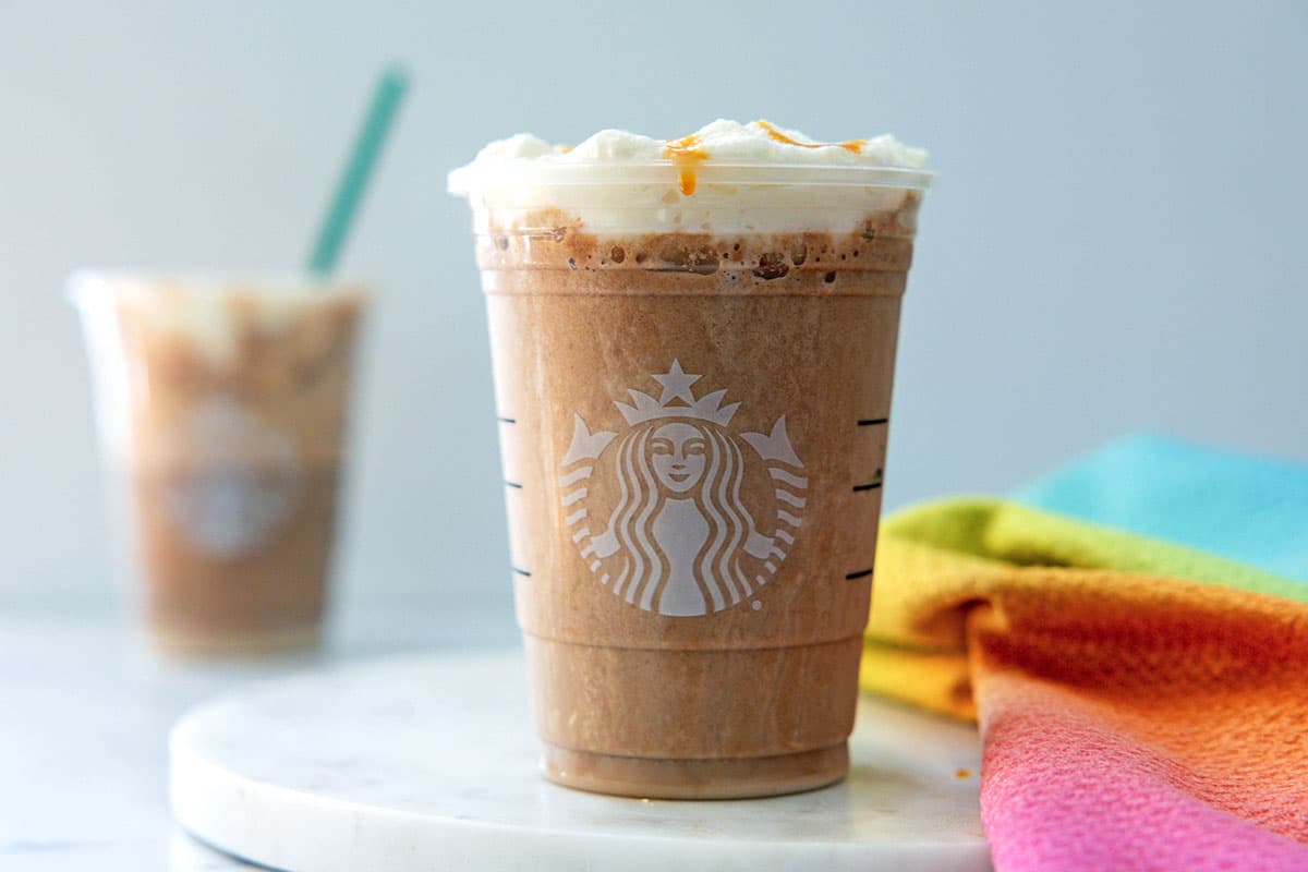 Landscape head-on view of a Salted Caramel Mocha Frappuccino with cold foam with second drink in background.