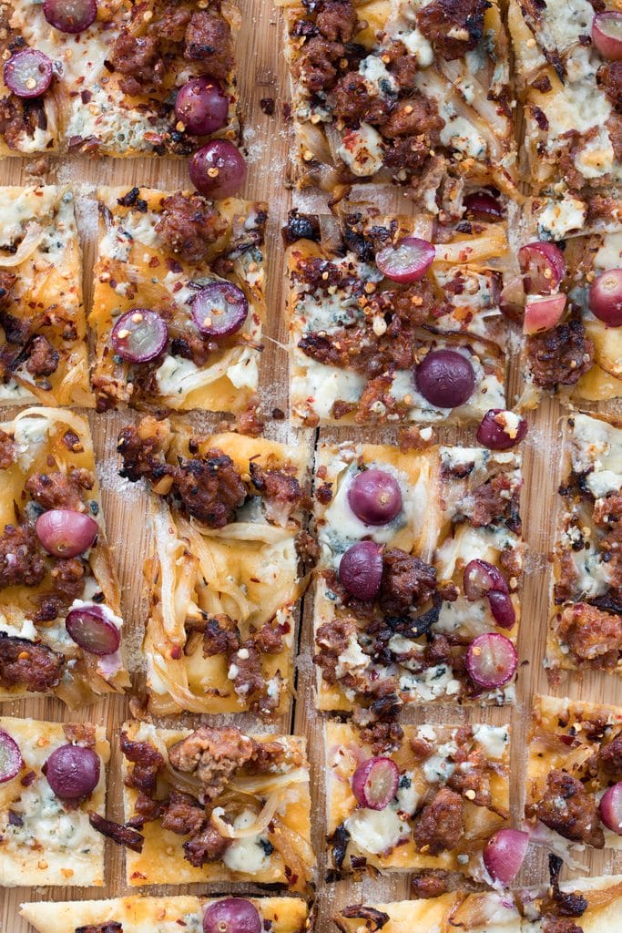 A shot from above showing various square slices of sausage, grape, and gorgonzola flatbread pizza