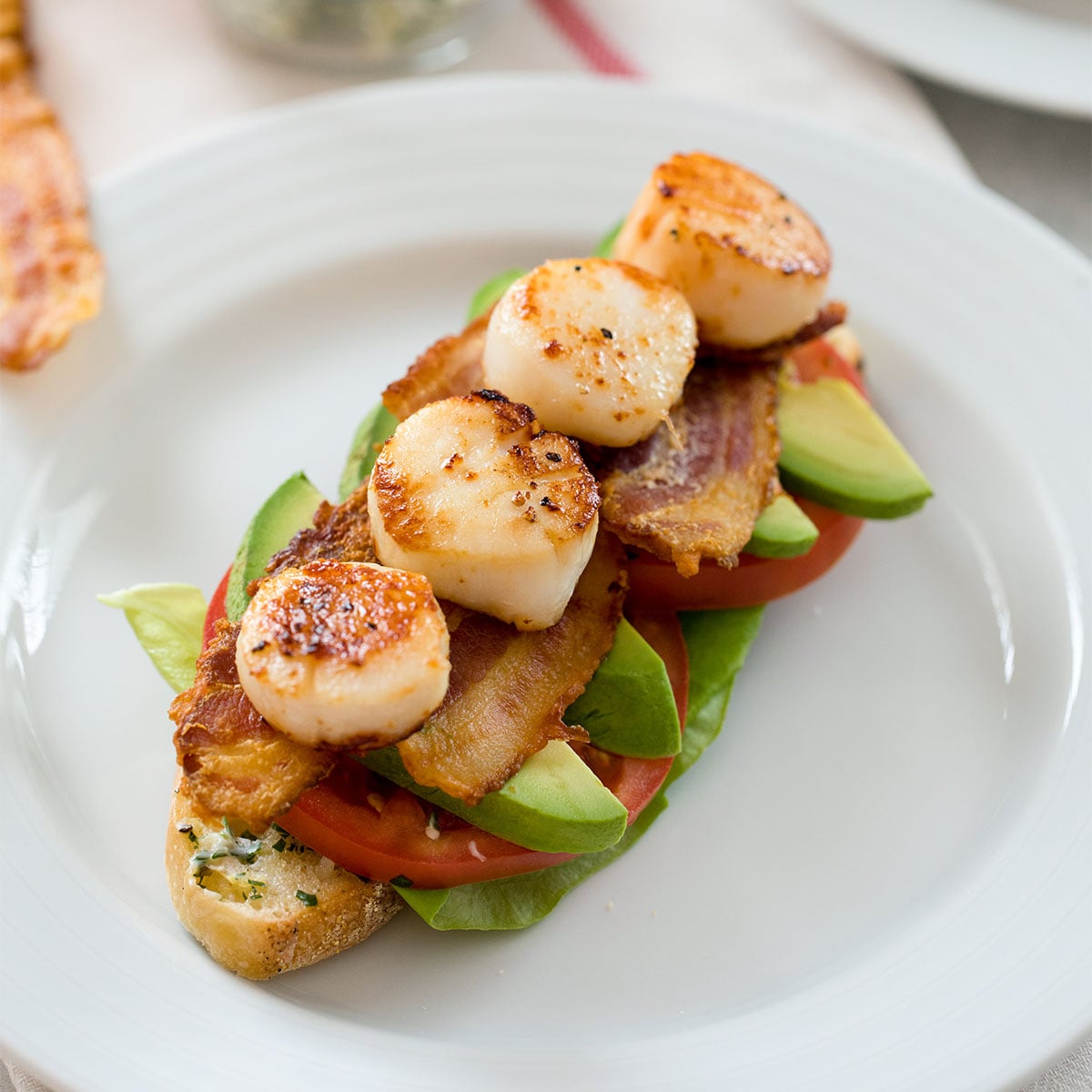 Closeup view of an open-faced seared scallop BLT sandwich.