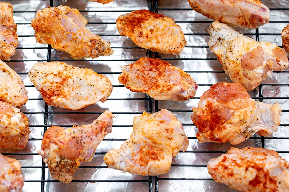 Chicken wings with seasoning on metal rack.