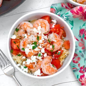 Overhead closeup view of a shrimp and feta orzo salad in a white bowl.