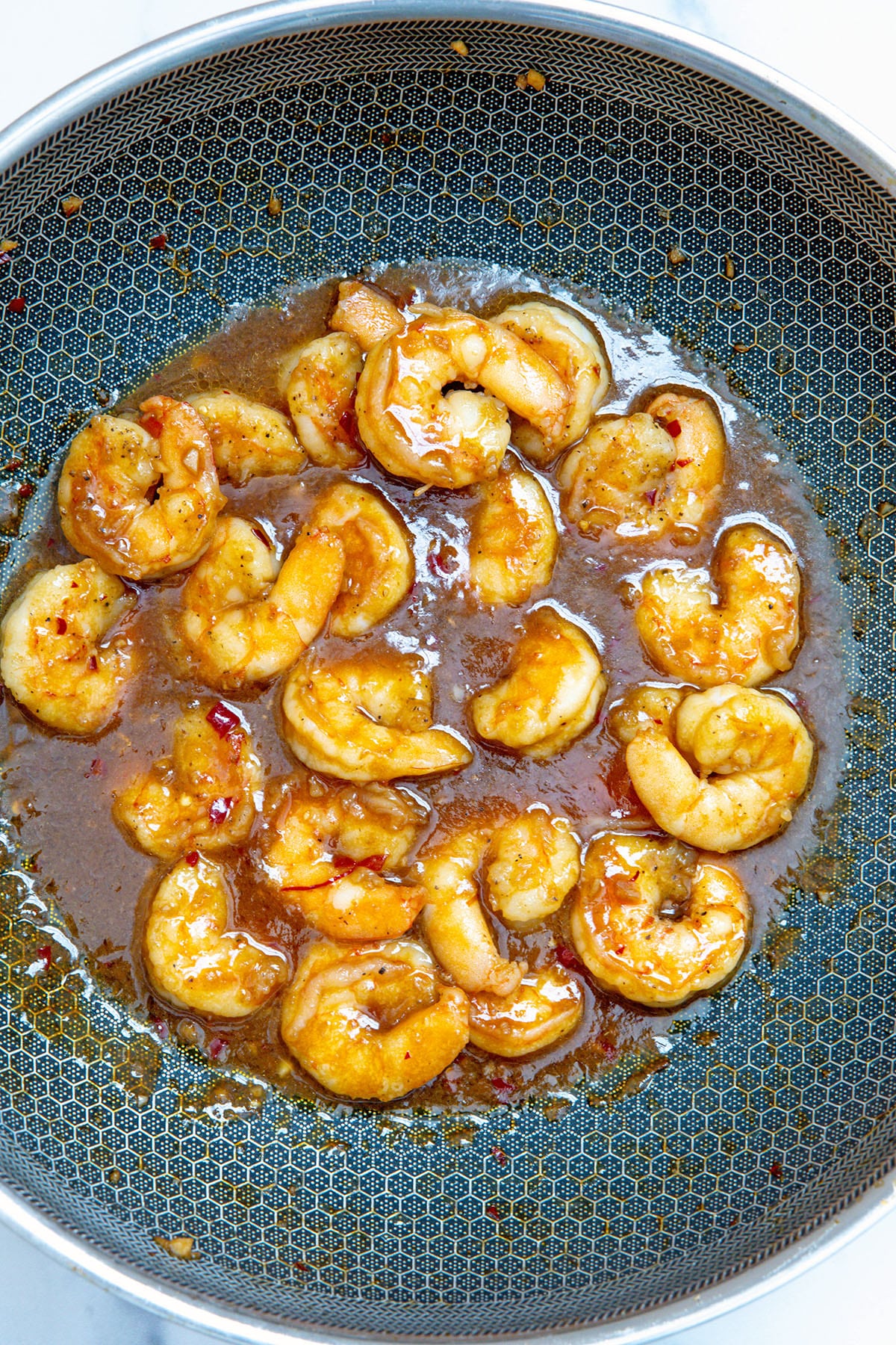 Overhead view of shrimp cooking in General Tso's sauce in wok.
