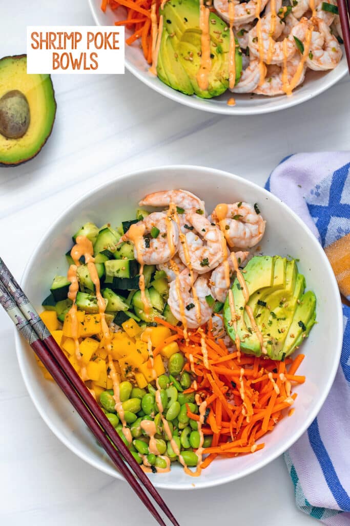 Overhead view of a shrimp poke bowl with shrimp ceviche, avocado, mango, edamame, carrots, cucumber, and sushi rice with chopsticks and the recipe title at the top.