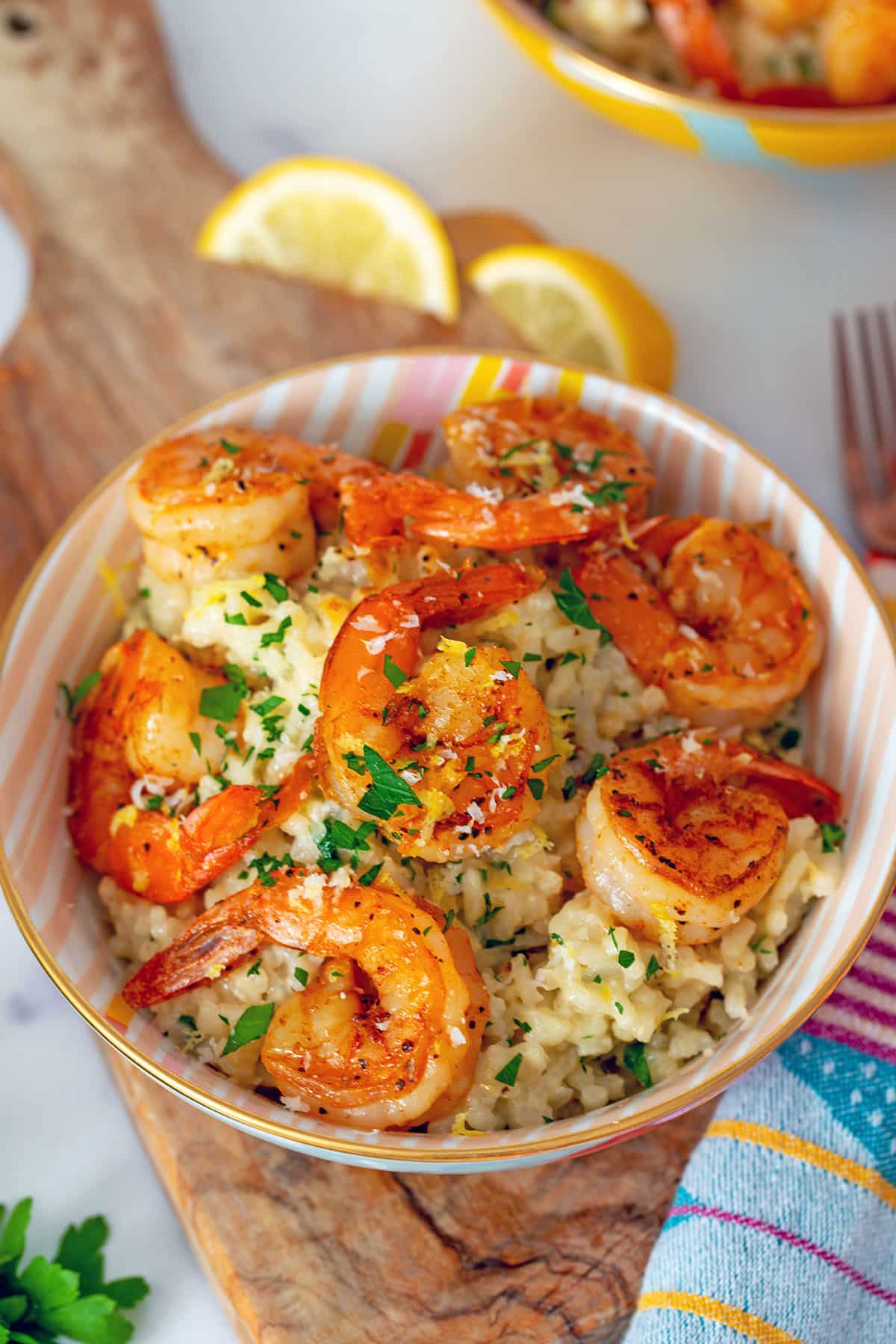 Closeup head-on view of risotto in bowl with shrimp on top with parsley and lemon in background.