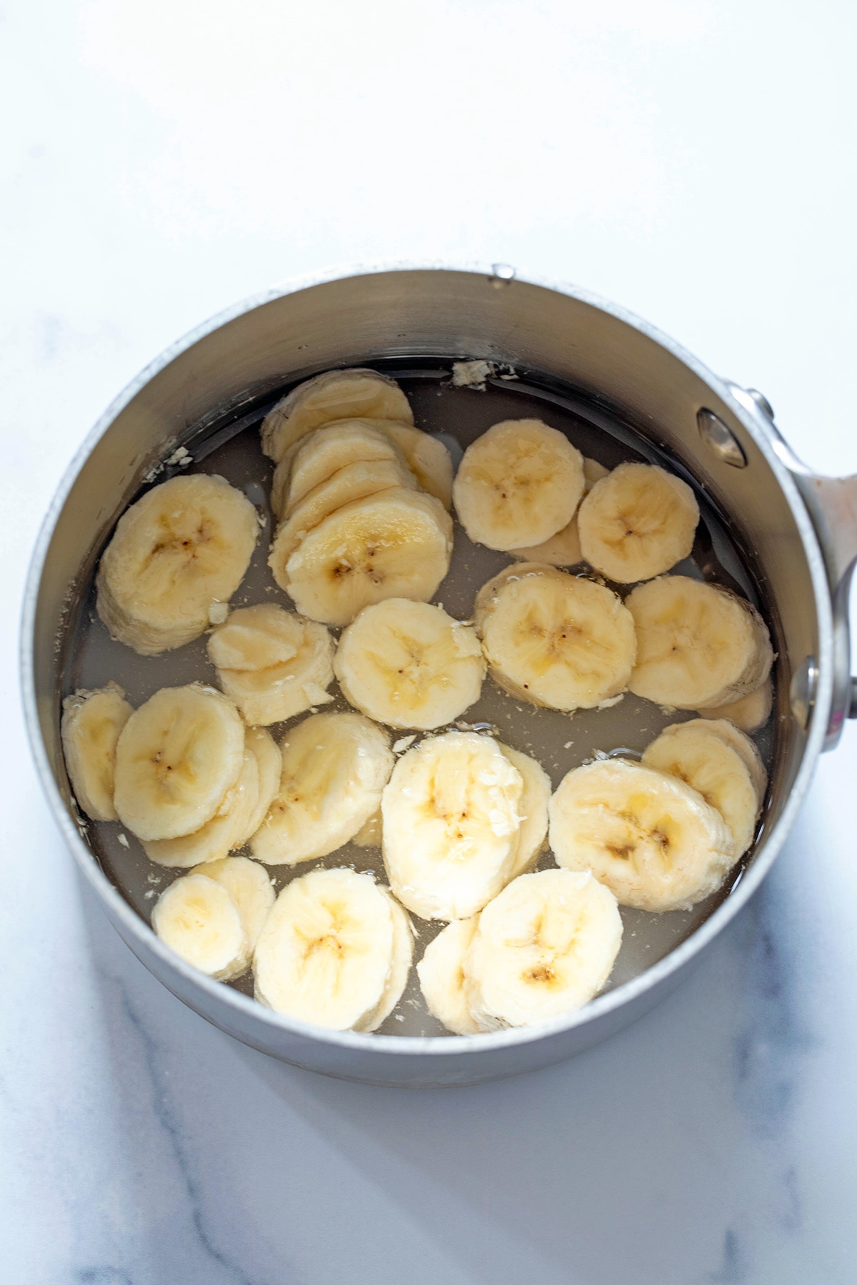 Sliced bananas in a saucepan with water and sugar.