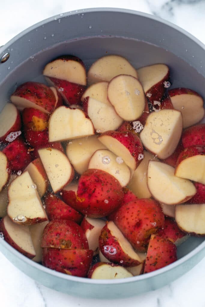 Quartered red skin potatoes covered in water in large pot.