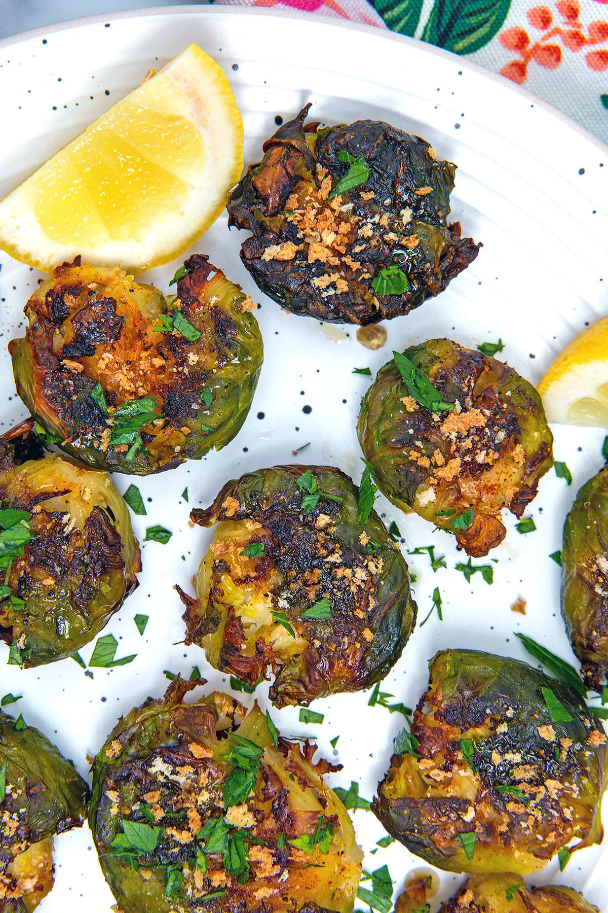Closeup view of smashed brussels sprouts on plate with lemon wedge.