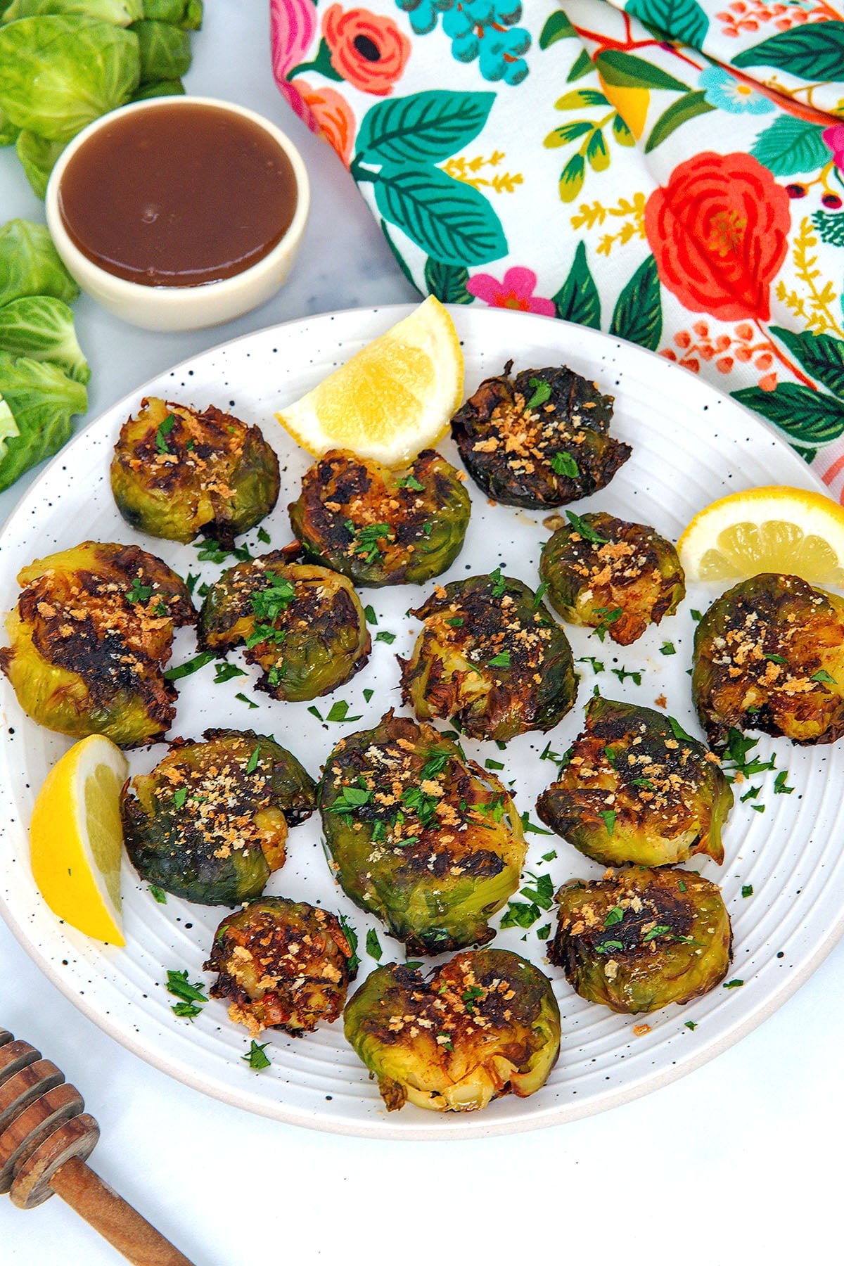 Smashed brussels sprouts on a plate with lemon wedges and dipping sauce in background.
