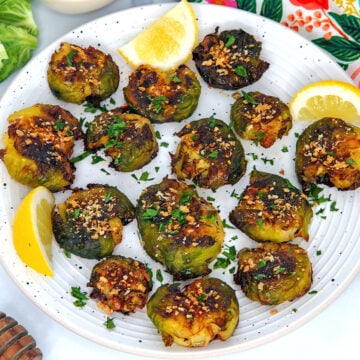 Closeup view of smashed brussels sprouts on a white plate with lemon wedges.