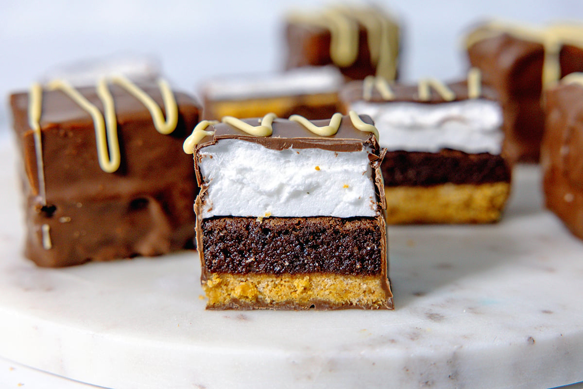 Landscape head-on view of a s'mores brownie bar with chocolate coating with more bars in the background.