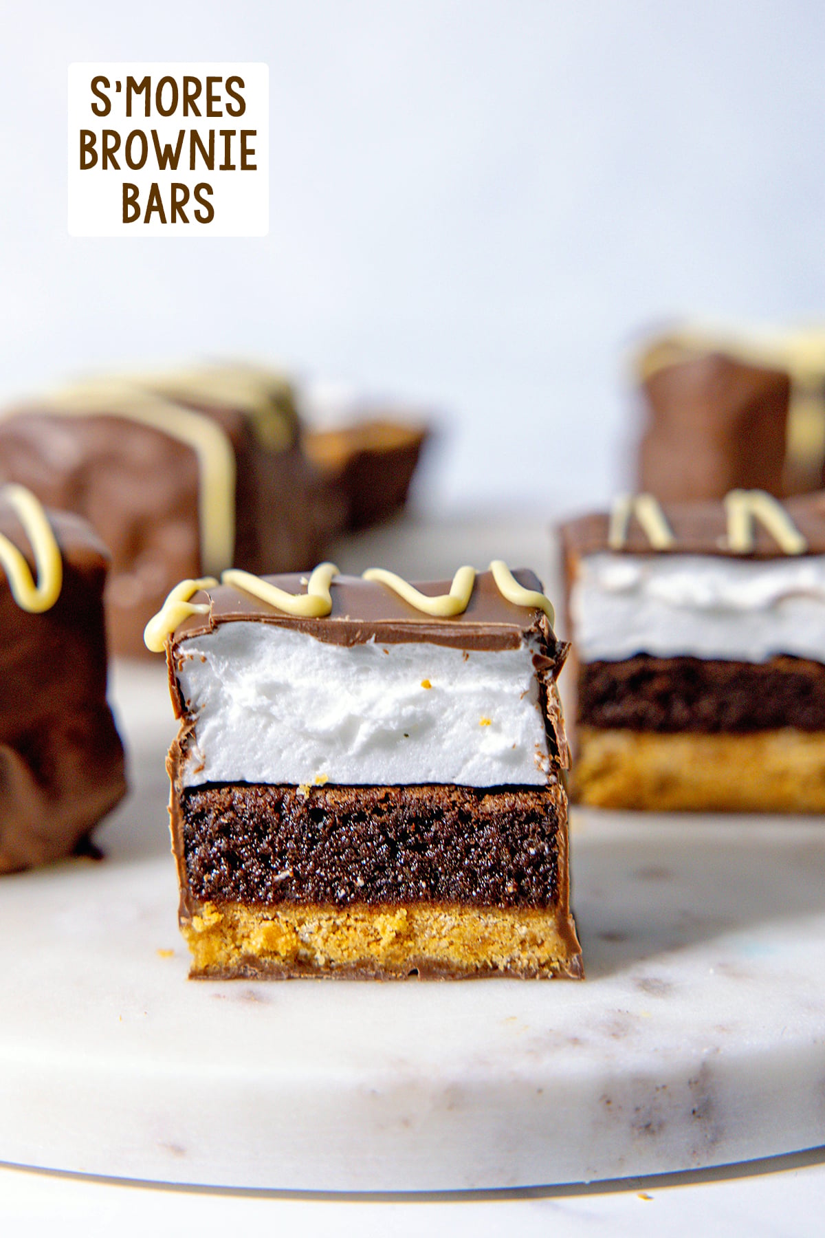 Head-on view of s'mores brownie bars with graham cracker, brownie, and marshmallow layer coated in chocolate with recipe title at top.
