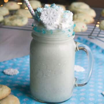 Closeup view of a sugar cookie milkshake with snowflake decoration and cookies in background.