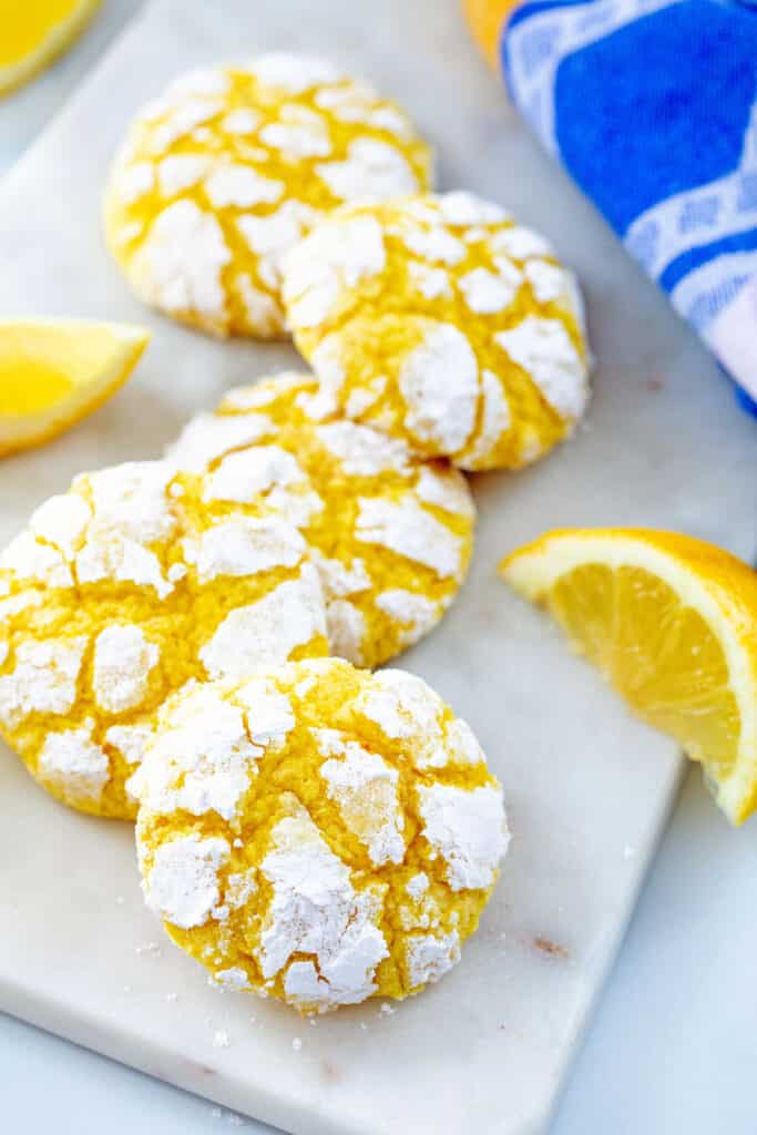 Overhead view of five soft lemon cookies on a marble platter with lemon slices all around.