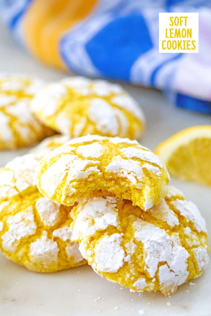 Soft lemon cookies with confectioners' sugar piled up with lemon wedge and recipe title in background.