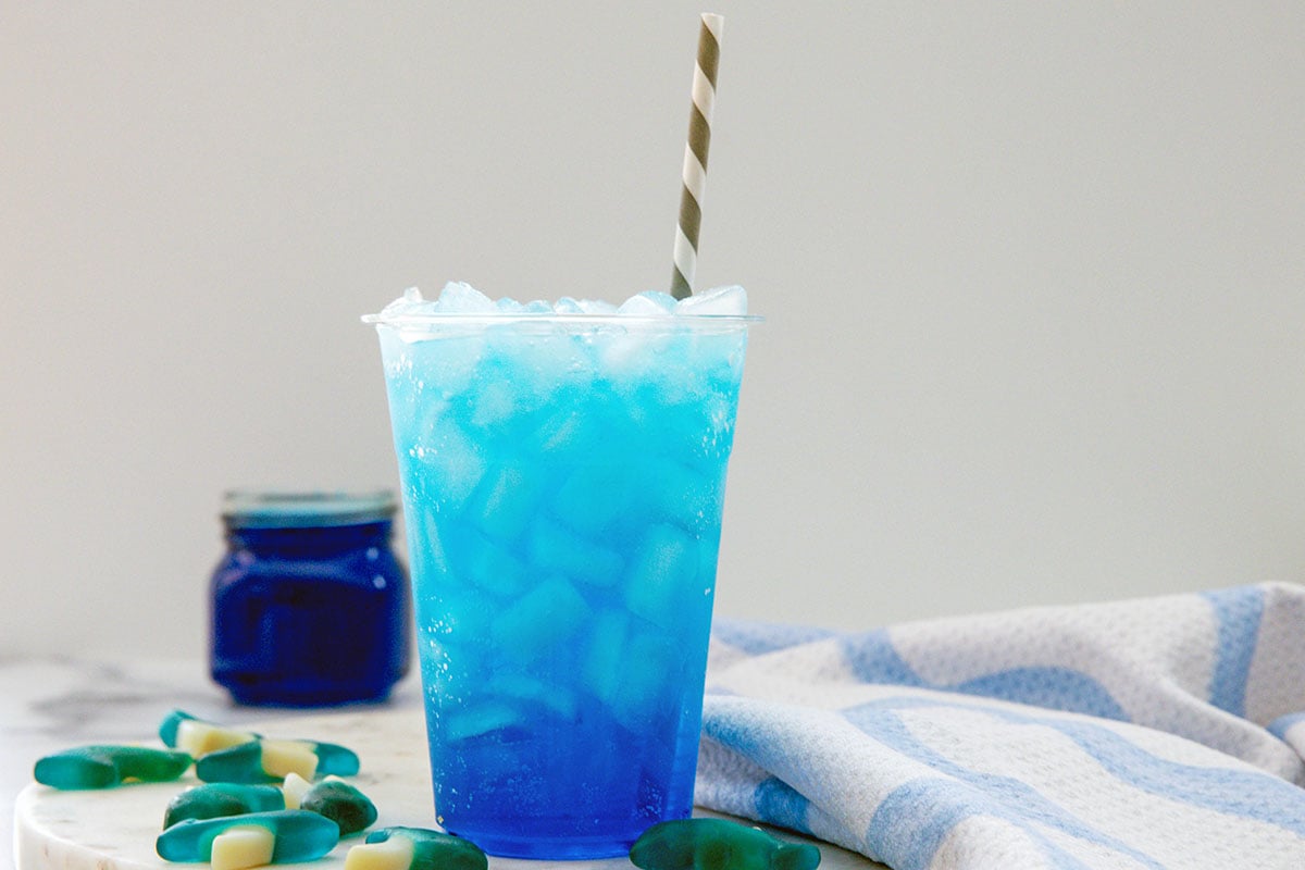Landscape head-on view of a Sonic Ocean Water drink with jar of blue coconut syrup and gummy sharks all around.