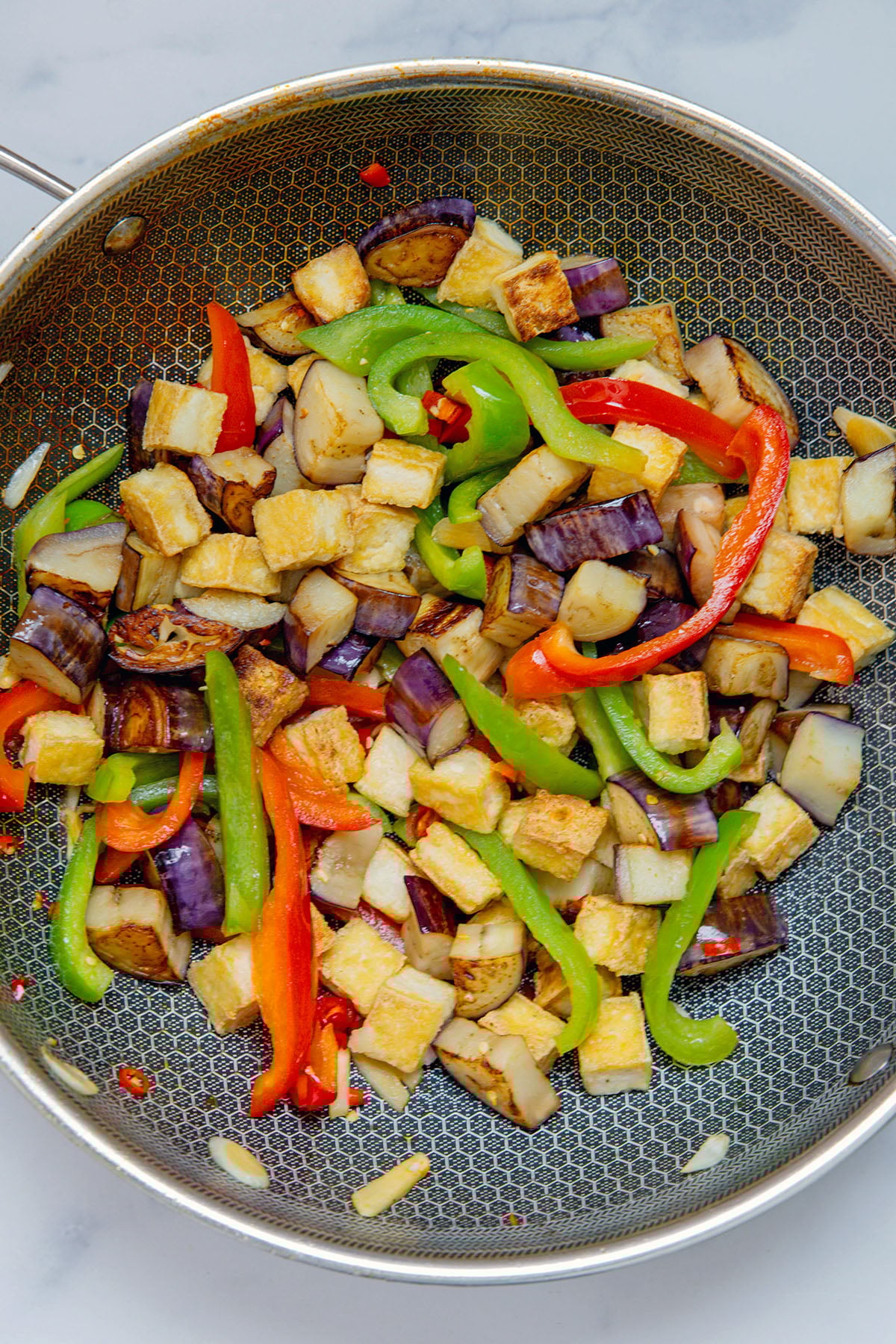 Eggplant, tofu, and bell peppers in wok.