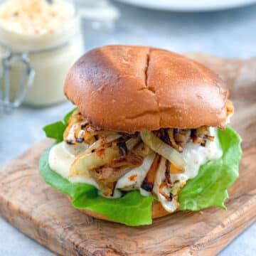 Head-on closeup view of a spicy cheesy chicken burger with caramelized onions and lettuce.