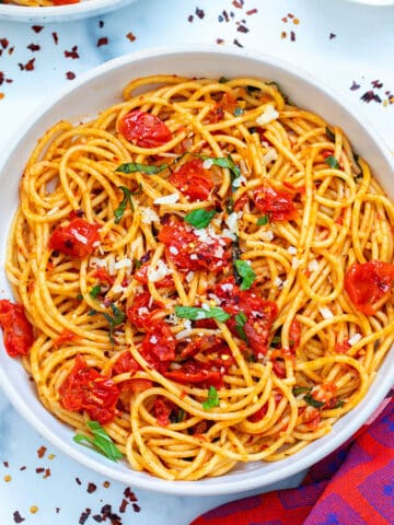 Overhead view of a bowl of spicy spaghetti with red pepper flakes all around.