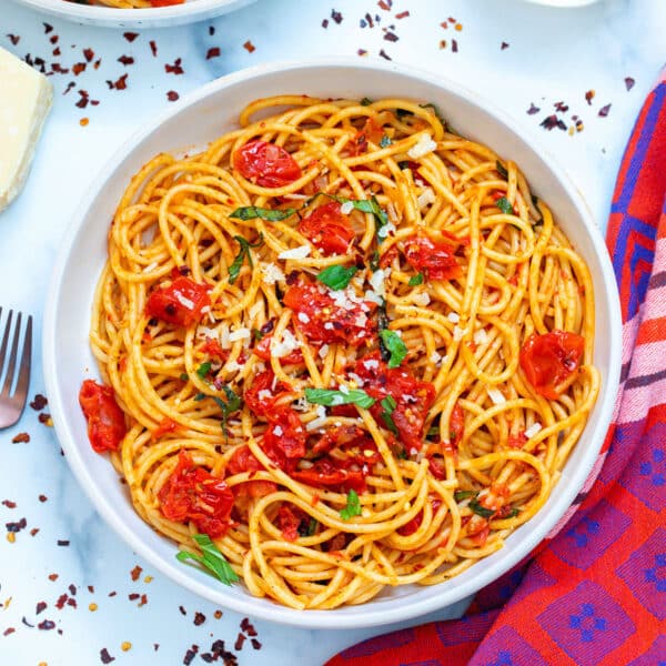 Overhead view of a bowl of spicy spaghetti with red pepper flakes all around.