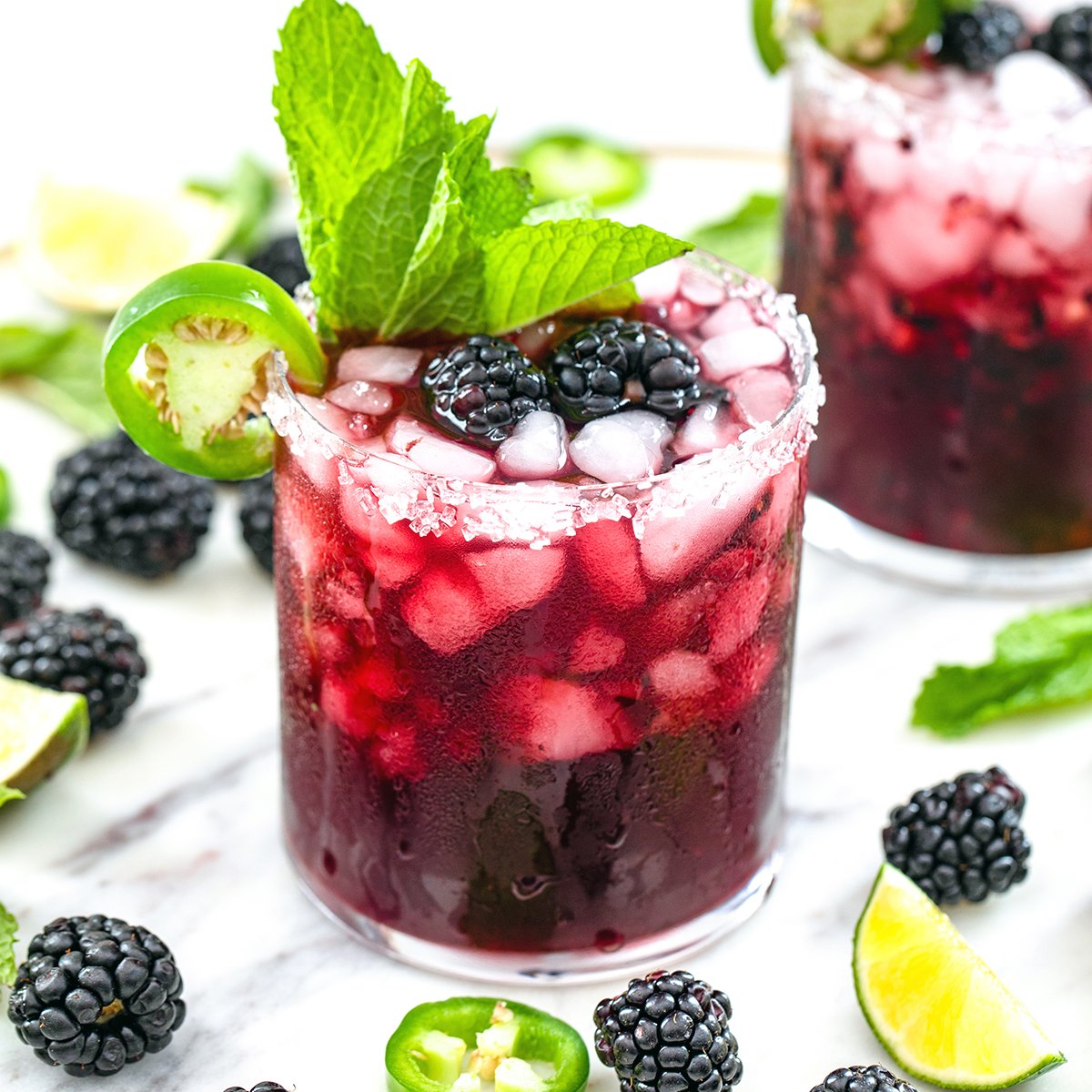 Closeup view of a spicy vodka blackberry smash in a glass with lots of mint, blackberries, jalapeño, and lime.