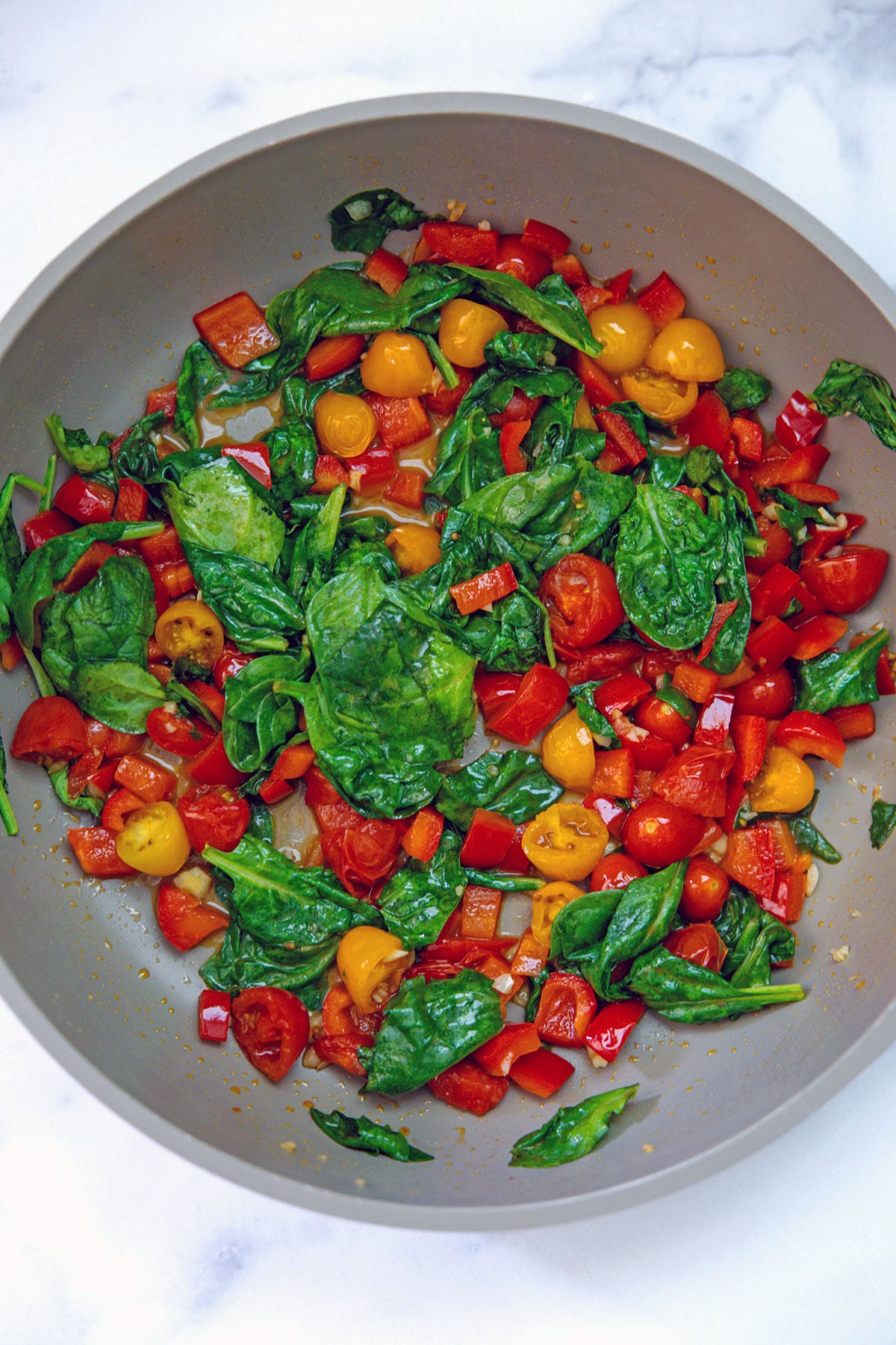 Tomatoes, red peppers, and spinach cooking in skillet.