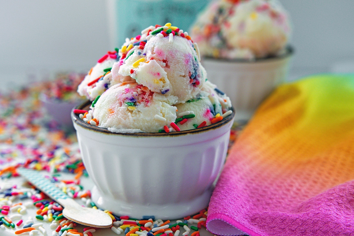 Head-on landscape closeup view of a bowl of a bowl of rainbow sprinkles ice cream.