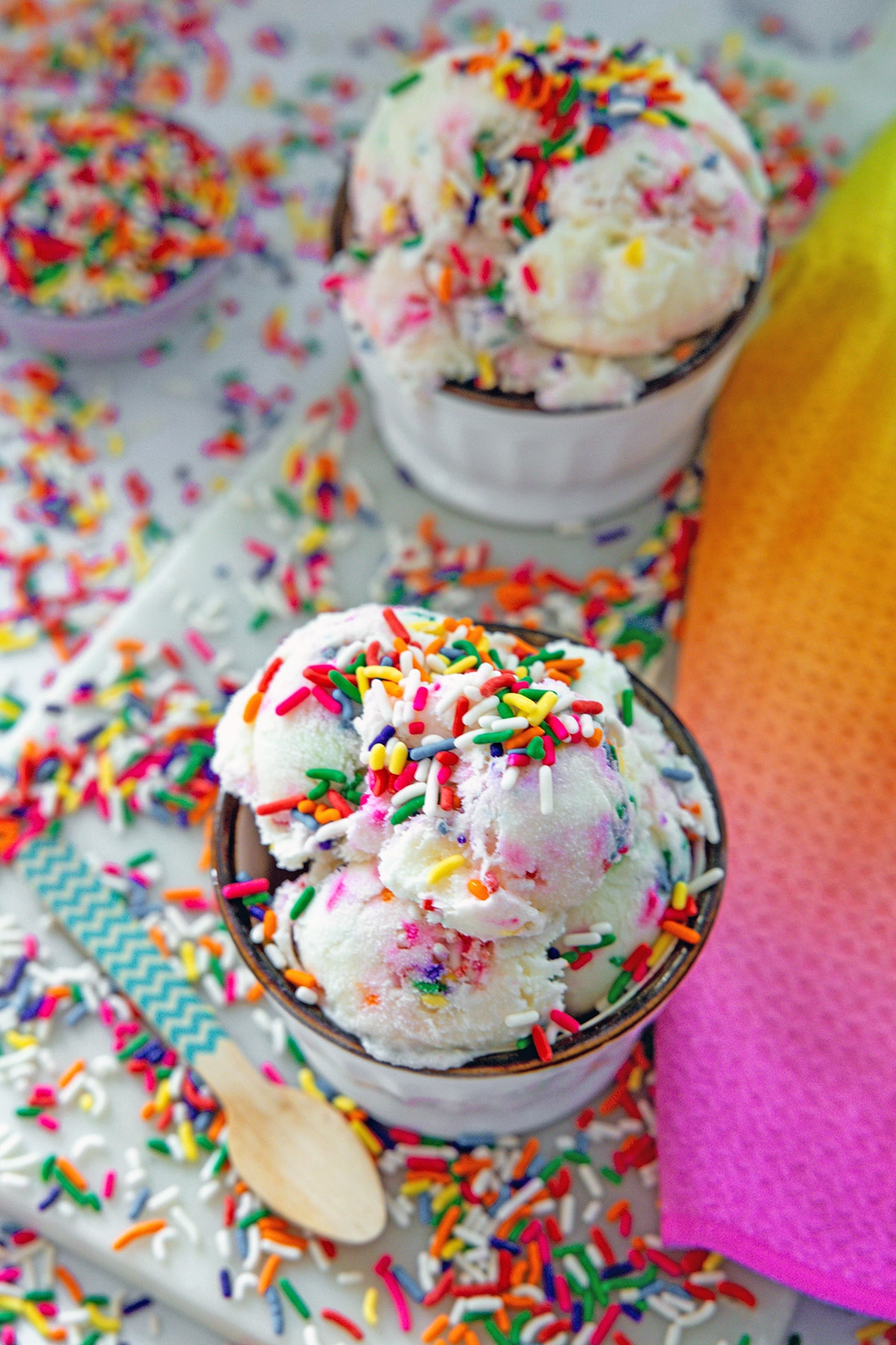Overhead view of two bowls of sprinkles ice cream with rainbow sprinkles all around.