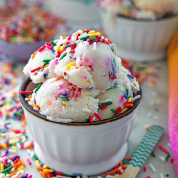 Closeup head-on view of a bowl of sprinkles ice cream with rainbow sprinkles all around.