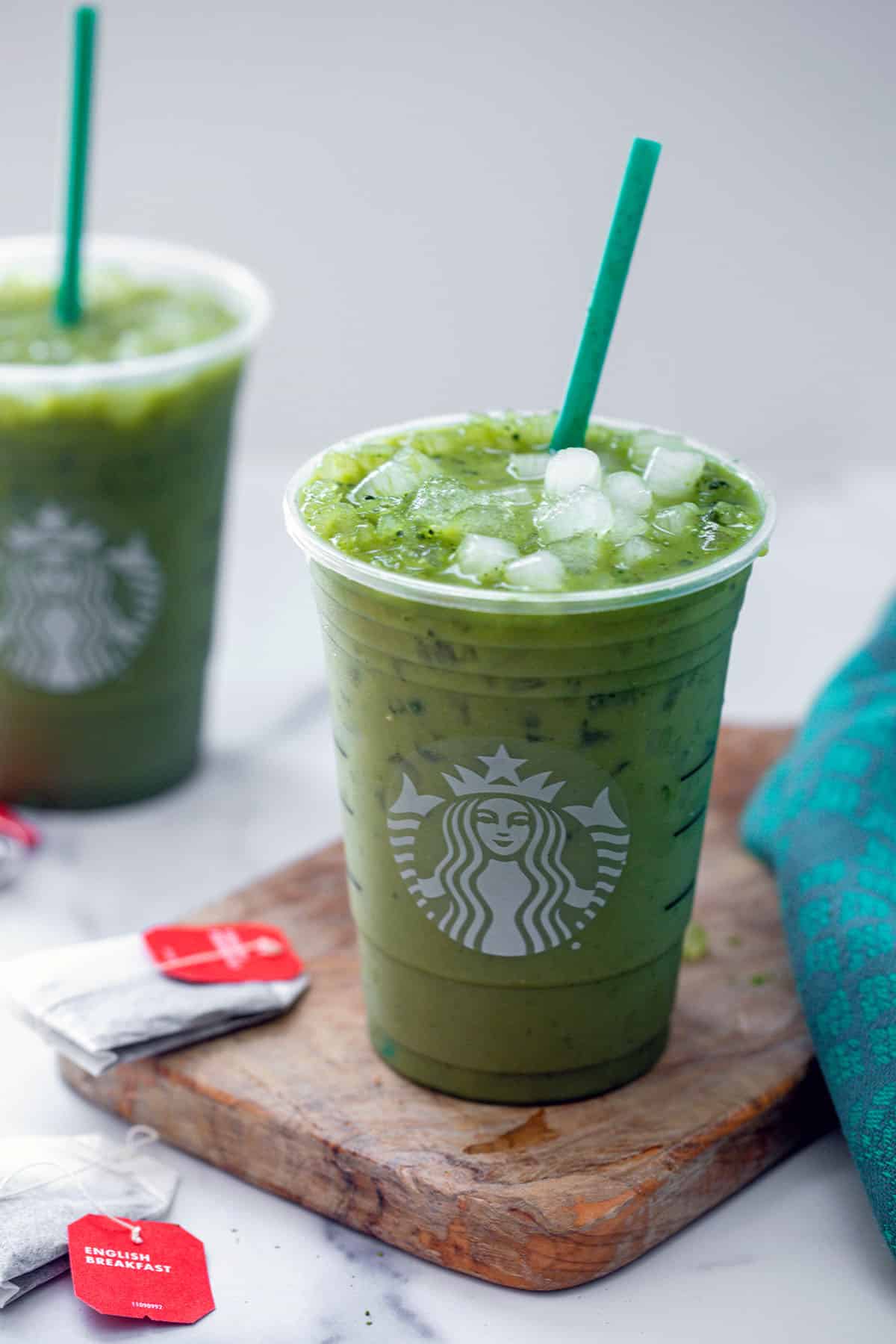 Overhead view of two Starbucks Green Drinks with green straws and black tea bags in background.