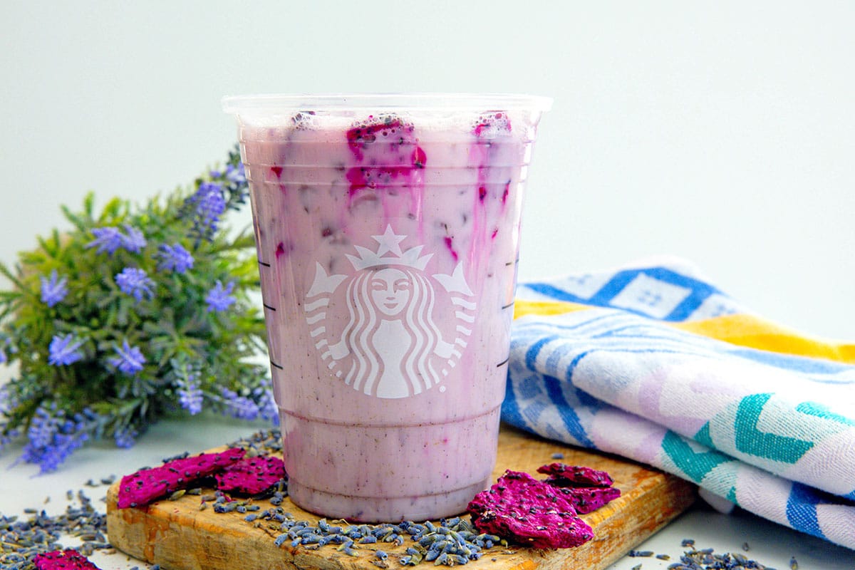 Landscape head-on view of a Lavender Oatmilk Chill in a Starbucks cup with freeze-dried lavender pieces all around.