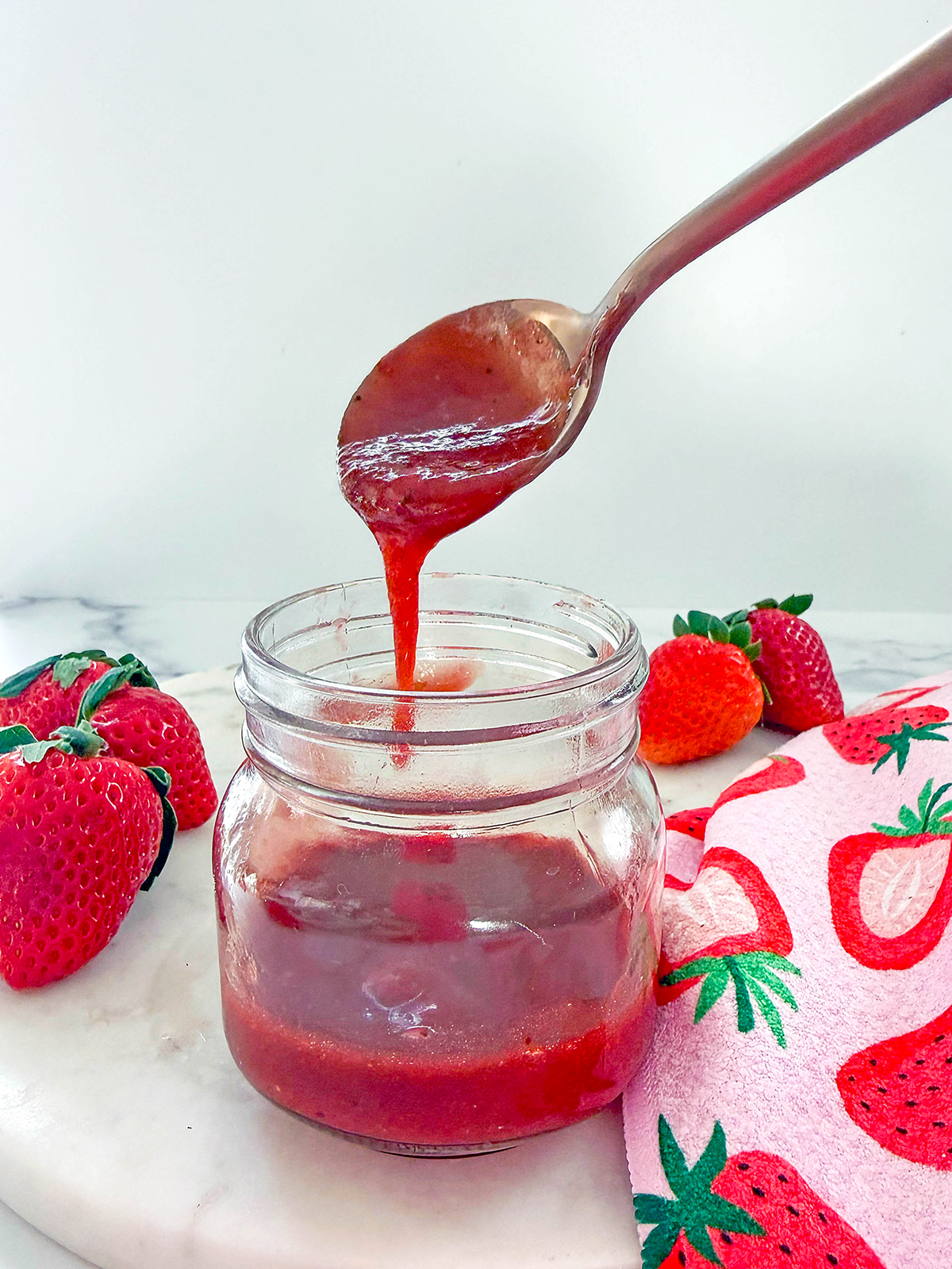 Small jar of Starbucks strawberry puree with spoon drizzling puree over it.