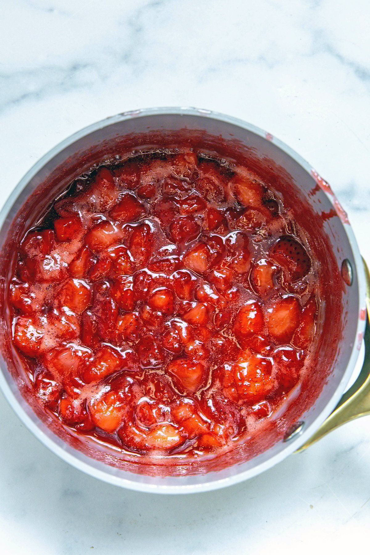 Overhead view of strawberries in saucepan with sugar and water turning jammy.