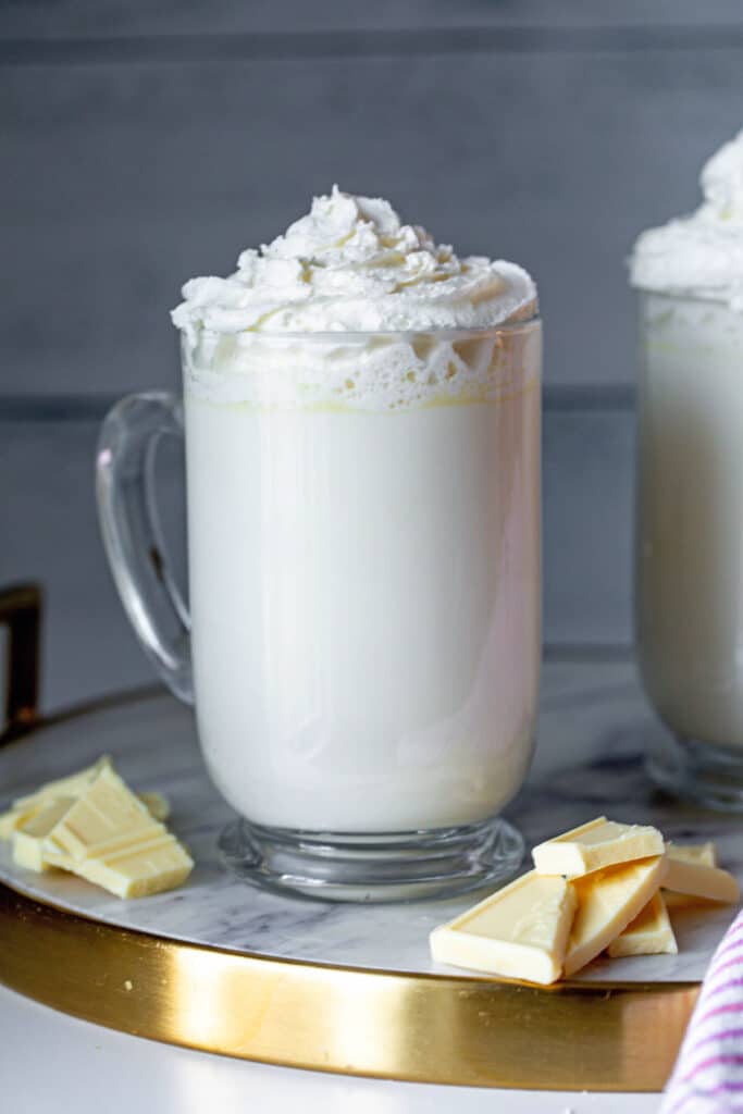 White hot chocolate like Starbucks in a clear mug with whipped cream and white chocolate pieces on the side.