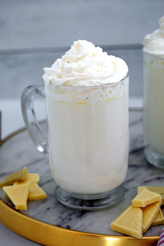 Head-on view of a mug of Starbucks white hot chocolate with whipped cream and white chocolate pieces on the side.