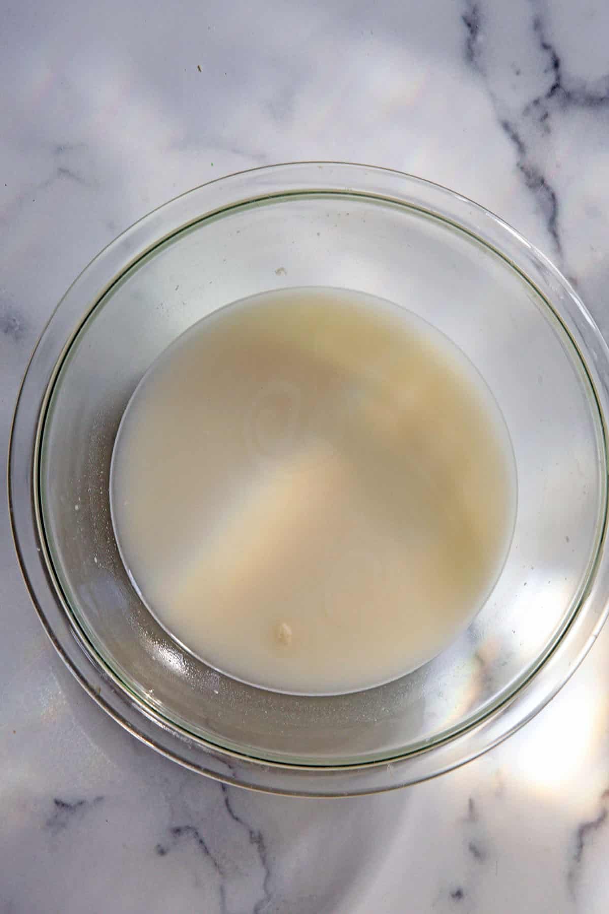 Overhead view of water, sourdough starter, and sugar mixed together in bowl.